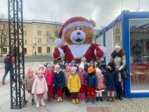 Zdjęcie grupowe dzieci i wychowawczyni na tle dużego misia w świątecznej czapce