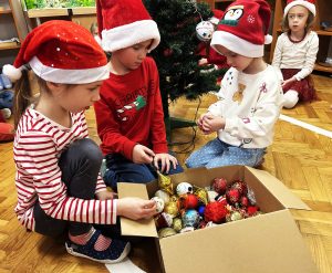 Dzieci ozdabiają choinkę bombkami.