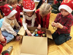 Dzieci ubierają choinkę kolorowymi bombkami.